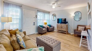 A living room with a sofa, ottoman, two armchairs, a television, a ceiling fan, and a wooden cabinet. - Coastal paradise with pool, beach access & central AC - near shops & dining (Gulf Shores)