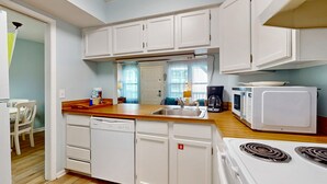 A compact kitchen with white cabinetry, a dishwasher, a microwave, and a stove. - Coastal paradise with pool, beach access & central AC - near shops & dining (Gulf Shores)