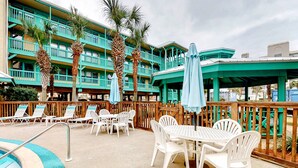 A pool area with lounge chairs and umbrellas, a pool, and a building with balconies. - Coastal paradise with pool, beach access & central AC - near shops & dining (Gulf Shores)