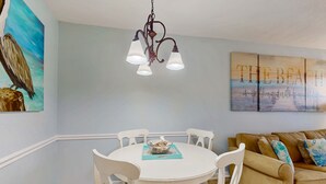 A dining area with a white table, chairs, and a hanging light fixture. - Coastal paradise with pool, beach access & central AC - near shops & dining (Gulf Shores)
