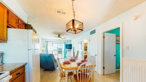A kitchen with wooden cabinets, a white refrigerator, a dining table with chairs, and a hanging light fixture. - Home with partial ocean view, central AC, washer/dryer & pool (Gulf Shores)