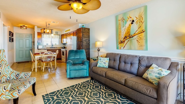 A living room with a sofa, teal armchair, dining table, and ceiling fan. - Home with partial ocean view, central AC, washer/dryer & pool (Gulf Shores)