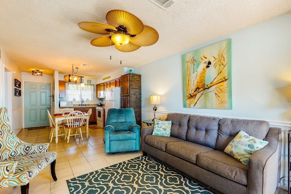 A living room with a sofa, teal armchair, dining table, and ceiling fan. - Home with partial ocean view, central AC, washer/dryer & pool (Gulf Shores)