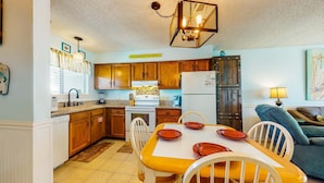 A kitchen with wooden cabinets, a dining table with chairs, a refrigerator, and a hanging light fixture. - Home with partial ocean view, central AC, washer/dryer & pool (Gulf Shores)