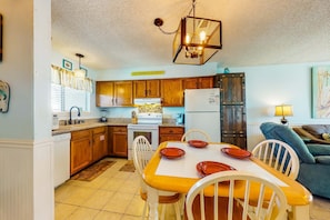 A kitchen with wooden cabinets, a dining table with chairs, a refrigerator, and a hanging light fixture. - Home with partial ocean view, central AC, washer/dryer & pool (Gulf Shores)