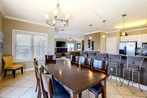 Un comedor amplio con una gran mesa y sillas, un candelabro y una cocina al fondo.