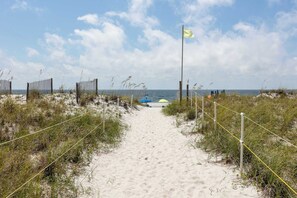 A sandy beach path with a flag, grass, and a boat in the distance. - Quaint Gulf front condo with outdoor pool, hot tub, sun deck - central location (Gulf Shores)