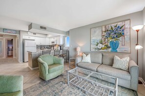A living room with a sofa, a green armchair, a coffee table, and a painting on the wall. - Quaint Gulf front condo with outdoor pool, hot tub, sun deck - central location (Gulf Shores)