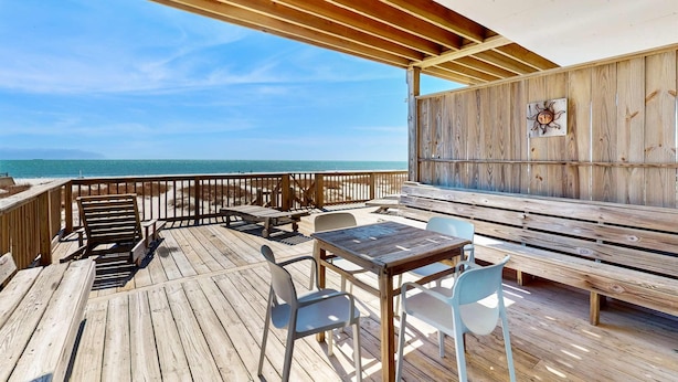 Una terraza de madera con mesas y sillas, con vista al océano.