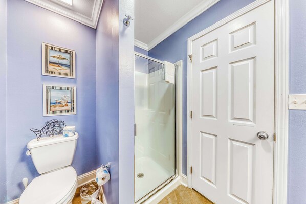 A bathroom with a toilet, a glass shower enclosure, and a white door. - Beachfront condo with amazing views, balcony, pools, hot tubs & fitness center (Gulf Shores)