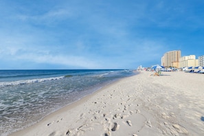 Ein Strand mit Fußabdrücken, einem klaren Himmel und Gebäuden im Hintergrund.