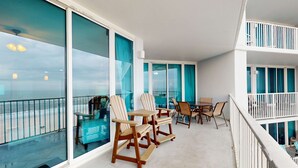 A balcony with large windows, a table with chairs, and a blue chair. - Beachfront condo w access to pools, hot tubs, sauna & fitness center (Gulf Shores)