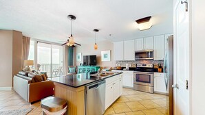 A modern kitchen with a central island, stainless steel appliances, and a dining area with a sofa. - Beachfront condo w access to pools, hot tubs, sauna & fitness center (Gulf Shores)