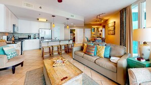 A spacious living area with a sofa, coffee table, and dining area. - Beachfront condo w access to pools, hot tubs, sauna & fitness center (Gulf Shores)