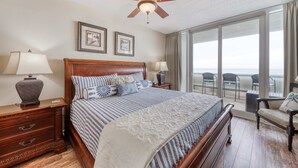 Une chambre d’hôtel avec un grand lit, un ventilateur de plafond, une table de chevet avec une lampe, une commode et une vue sur le balcon.