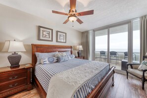 Ein Hotelzimmer mit einem großen Bett, einem Deckenventilator, einem Nachttisch mit Lampe, einem Schminktisch und Blick auf den Balkon.