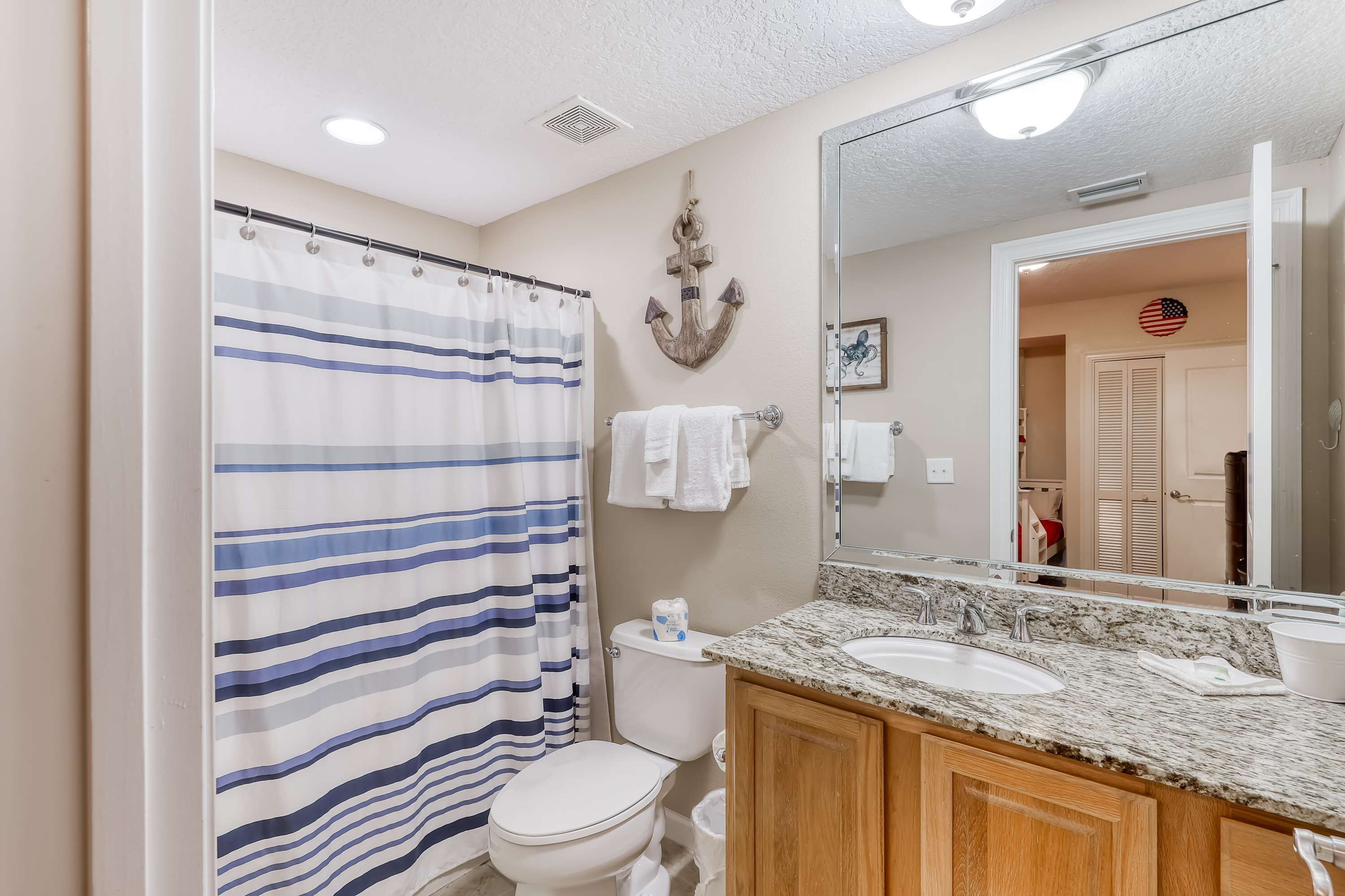 Une salle de bain avec un rideau de douche à rayures, des toilettes, un lavabo avec un miroir et des meubles en bois.