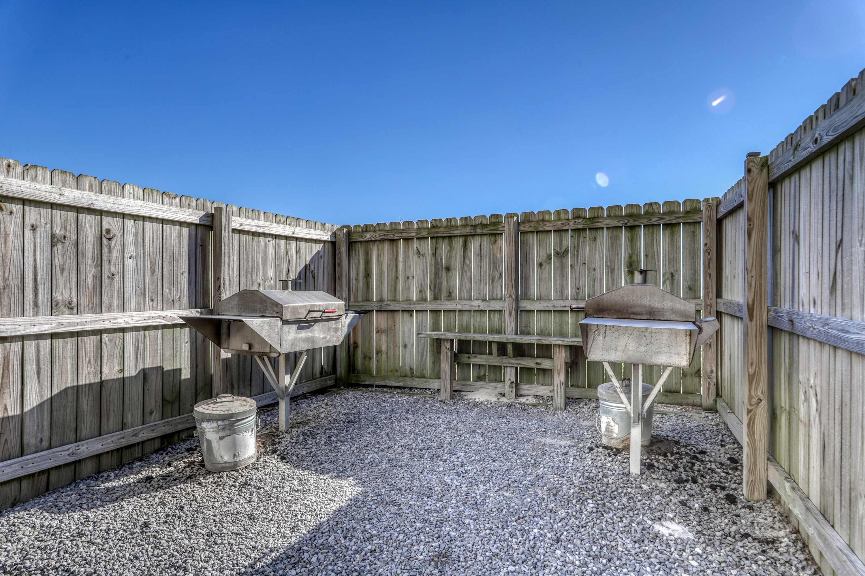 Een houten terras buiten met een grill en een barbecueplaats, omgeven door een houten omheining.