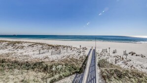 Une plage avec une promenade pavée menant à l’eau, entourée de dunes de sable et d’une végétation clairsemée.