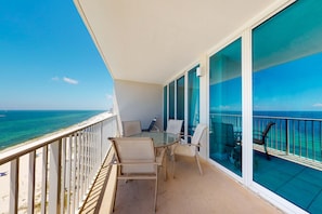 A balcony with a glass door, a round table, and two chairs. - Gulf-front condo w shared pools, hot tubs, sauna & beach access (Gulf Shores)
