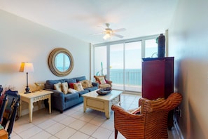 A living room with a sofa, coffee table, and wicker chair. - Gulf-front condo w shared pools, hot tubs, sauna & beach access (Gulf Shores)