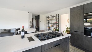 A modern kitchen with a central island, a dining area with a table and chairs, and a built-in bookshelf. - Villa with Pool, Spa, and Sauna (Saint-Nazaire-d'Aude)