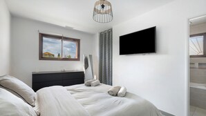 A bedroom with a bed, a TV mounted on the wall, a window, and a door. - Villa with Pool, Spa, and Sauna (Saint-Nazaire-d'Aude)