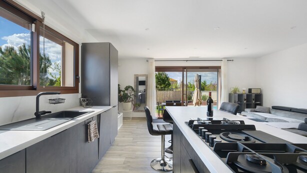 A modern kitchen with a large island, a built-in oven, and a view to the outdoor patio. - Villa with Pool, Spa, and Sauna (Saint-Nazaire-d'Aude)