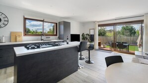 A modern kitchen with a central island, a dining area with a table and chairs, and a sliding glass door leading to a patio. - Villa with Pool, Spa, and Sauna (Saint-Nazaire-d'Aude)