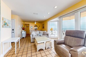 A living room with a sofa, a coffee table, and a chair. There is a door leading to another room and a window with a view. - Beachfront home on the dunes w/ amazing Gulf views & shared pool (Gulf Shores)