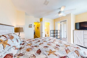 A bedroom with a bed, a ceiling fan, a TV, and a door leading to a bathroom. - Beachfront home on the dunes w/ amazing Gulf views & shared pool (Gulf Shores)