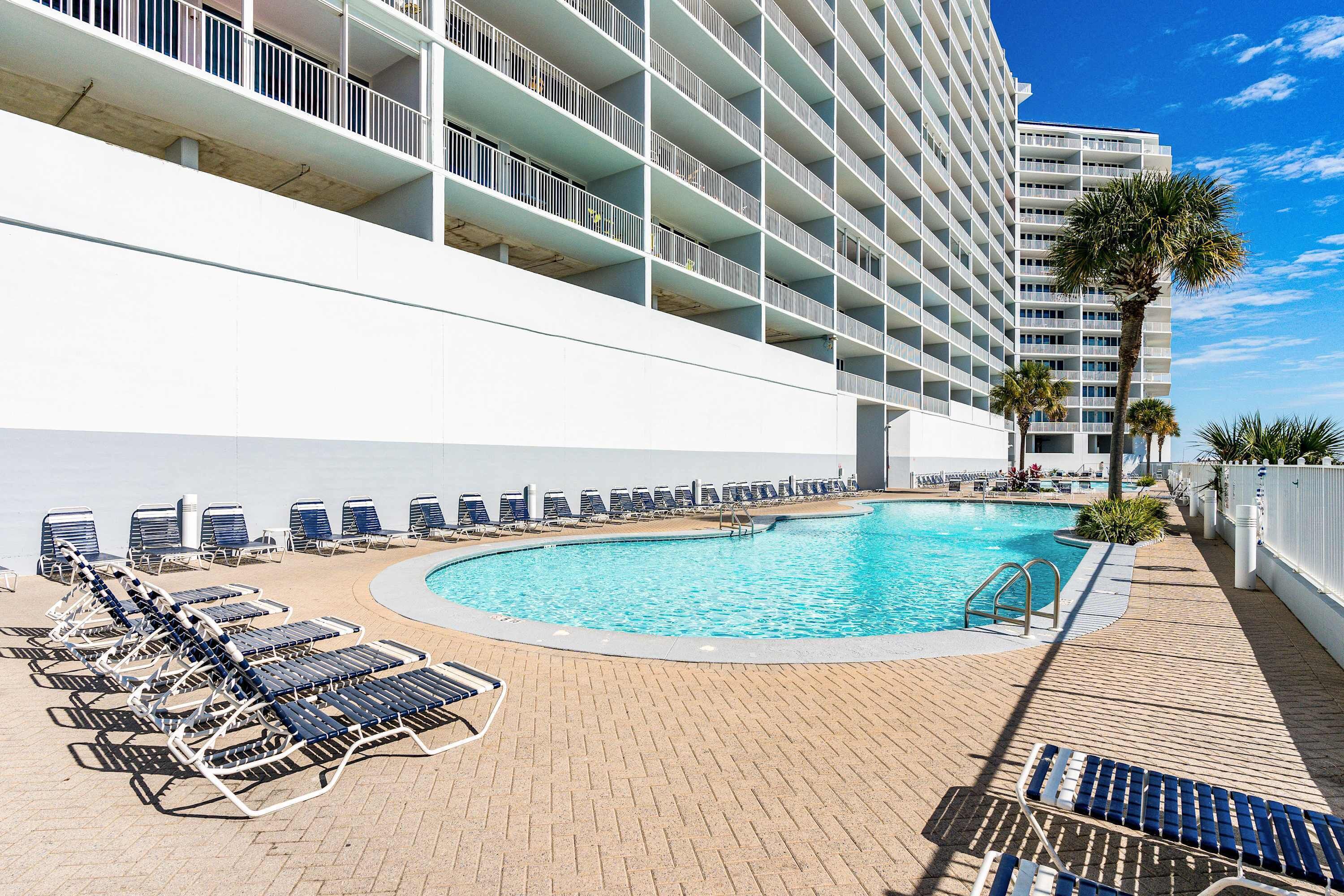 Un espace piscine d’hôtel avec des chaises longues, une piscine et un immeuble de grande hauteur en arrière-plan.
