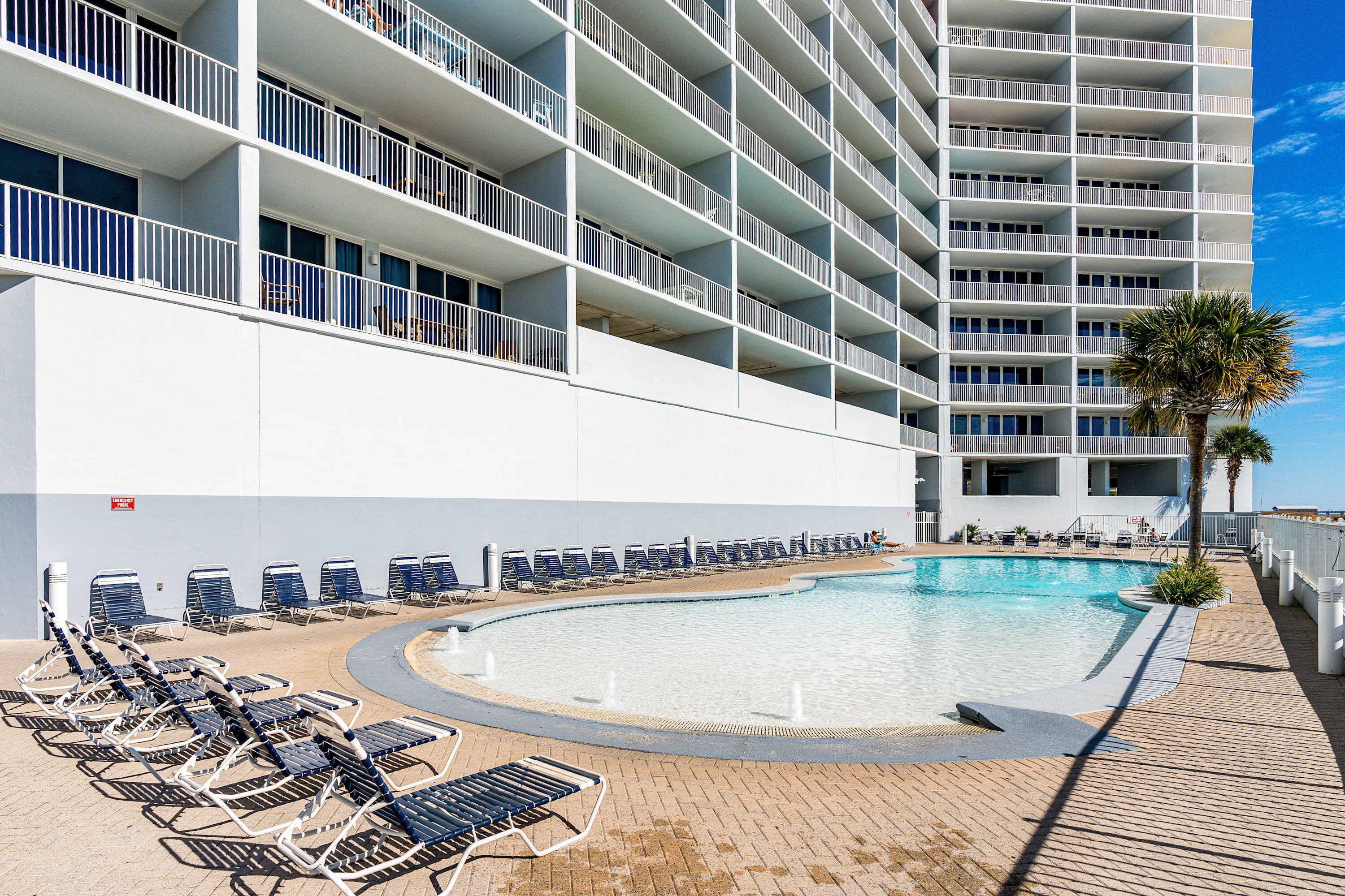 A hotel with multiple balconies, a swimming pool, and sun loungers.