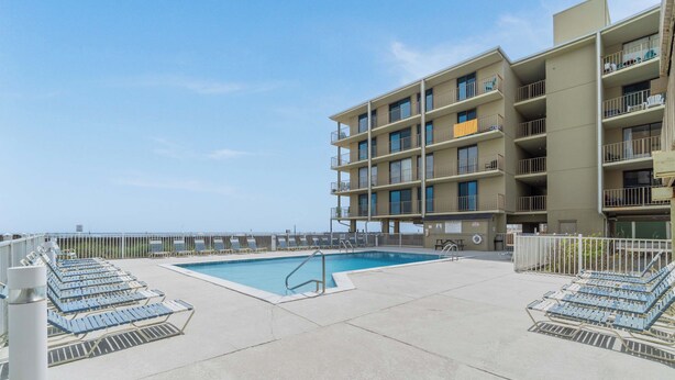 A pool area with lounge chairs and a building with multiple balconies. - Beachfront condo with balcony overlooking Gulf of Mexico & resort pool (Gulf Shores)