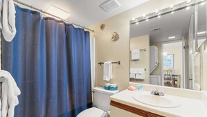 A bathroom with a shower curtain, toilet, sink, and a mirror with lights. - Beachfront condo with balcony overlooking Gulf of Mexico & resort pool (Gulf Shores)