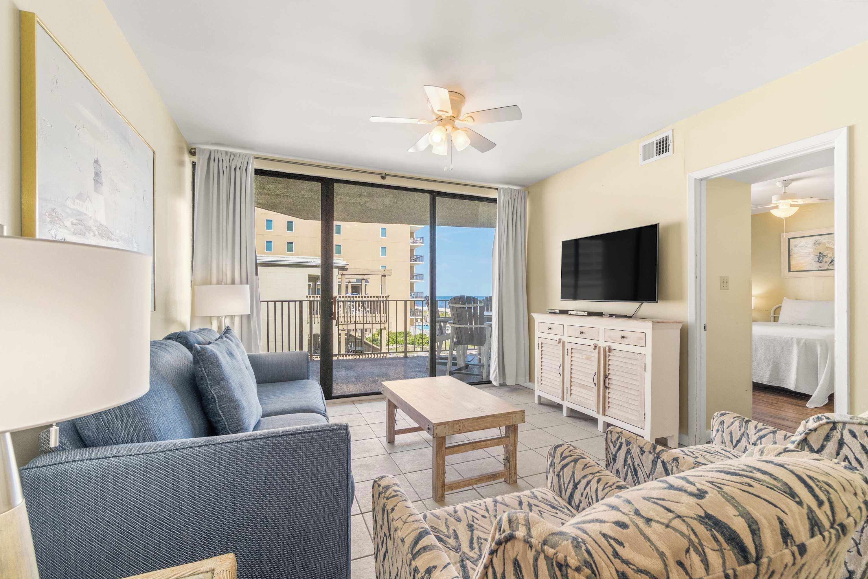 A living room with a sofa, a table, a TV, and a balcony with a view of buildings.