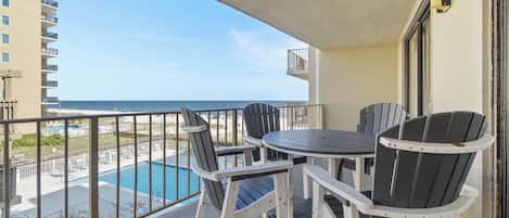 A balcony with a pool view, outdoor seating, and a clear sky.