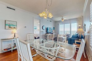 A living room with a glass dining table, white chairs, a ceiling fan, and a view of the ocean. - Penthouse-level, waterfront condo with epic Gulf-view balcony, pools, & gym (Gulf Shores)