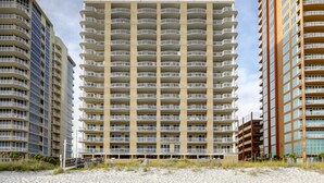 Un hotel moderno de gran altura con varios balcones, vista a la playa y un primer plano de arena.
