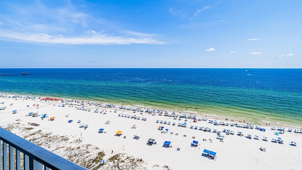 A beach with numerous umbrellas and chairs, a clear sky, and calm sea. - Well decorated Gulf-front condo with pool & hot tub access (Gulf Shores)
