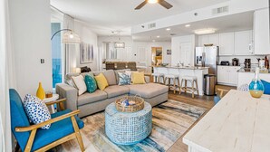 A modern living room with a sofa, a round coffee table, and a dining area with a table and chairs. - Well decorated Gulf-front condo with pool & hot tub access (Gulf Shores)