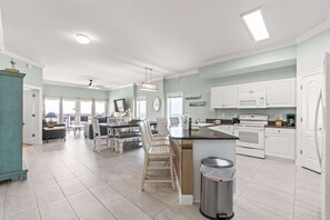 A spacious kitchen with white cabinets, a central island, and a dining area with chairs and a table. - Gulf-front condo with balcony overlooking beach, pool, new furniture, & W&D (Gulf Shores)