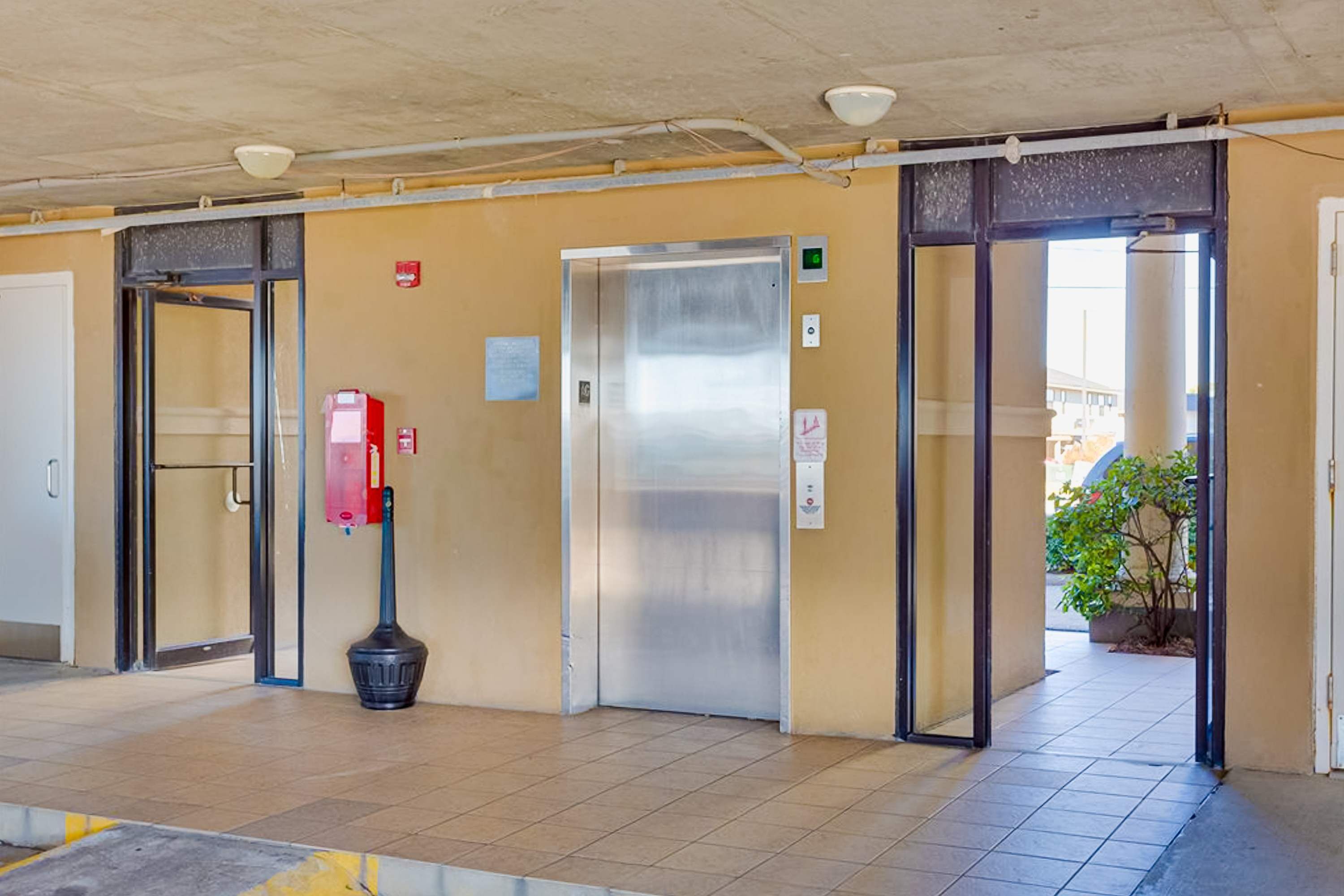 An indoor area with an elevator, a fire extinguisher, and a trash bin.