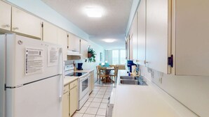 Eine Küche mit weißen Schränken, einem Kühlschrank, einem Herd und einer Essecke mit Tisch und Stühlen.