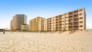 Ein Hotel direkt am Strand mit mehreren Etagen, Balkonen und einem Sandstrand im Vordergrund.