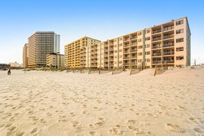 Een strandhotel met meerdere verdiepingen, balkons en een zandstrand op de voorgrond.