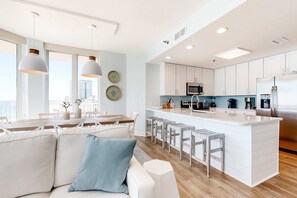 A modern kitchen with white cabinets, a central island, and bar stools. - Gulf-Front Corner Condo w Amazing Views, Huge Deck & Shared Pools, Hot Tubs (Gulf Shores)