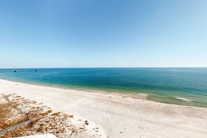A beach with clear water, a sandy shore, and a pier in the distance. - Gulf-Front Corner Condo w Amazing Views, Huge Deck & Shared Pools, Hot Tubs (Gulf Shores)