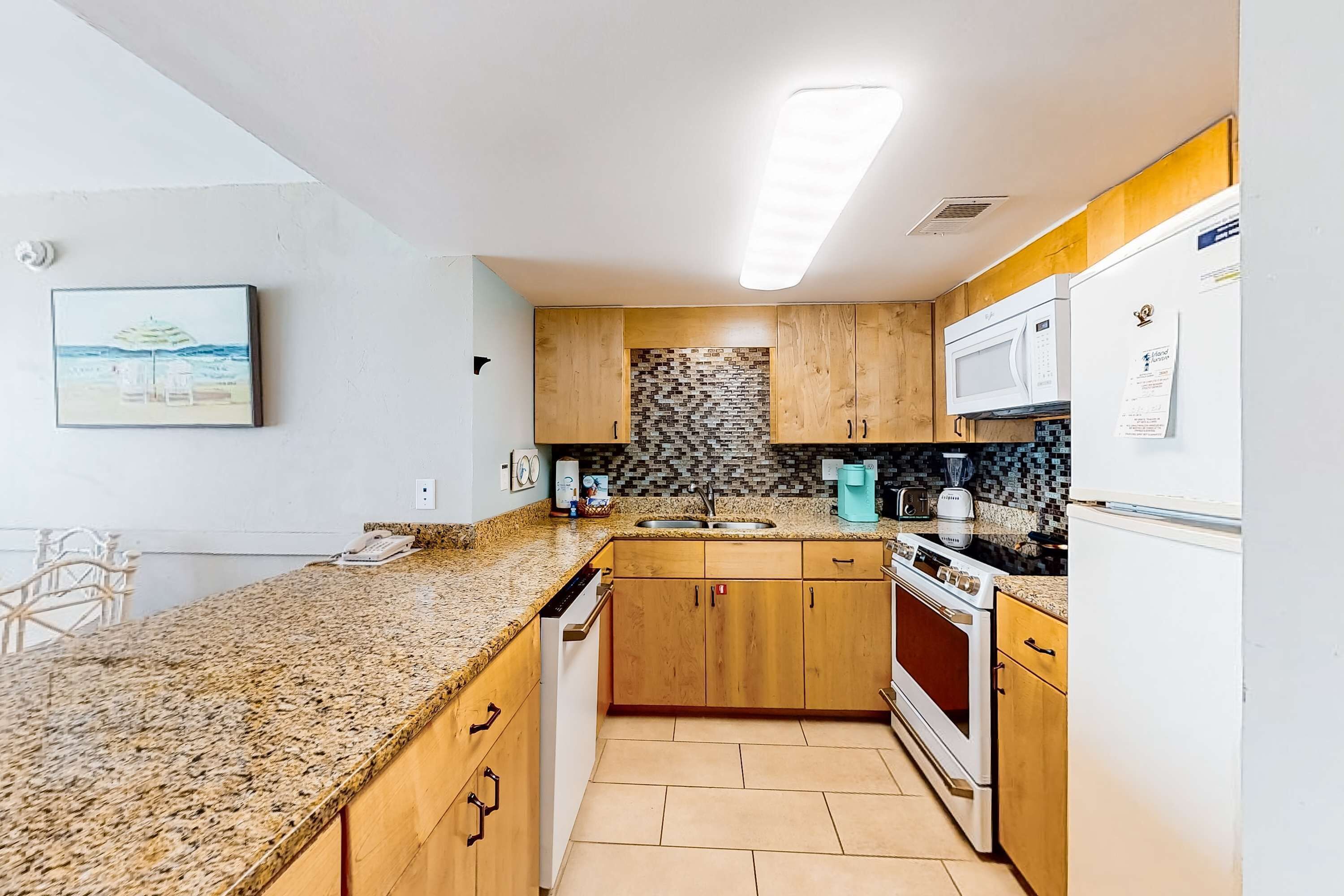 Una cocina con encimeras de granito, armarios de madera, microondas, estufa y refrigerador.