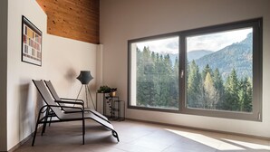 Una habitación moderna con un ventanal grande, una butaca reclinable, una lámpara de pie y un cuadro en la pared.